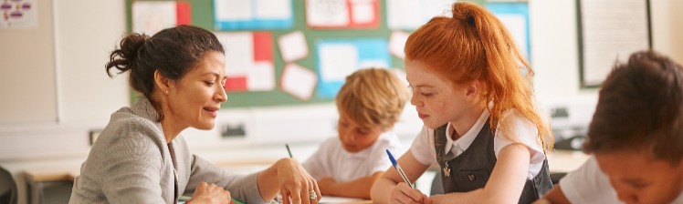 teacher and young student across a desk looking down at pieces of paper, smiling
