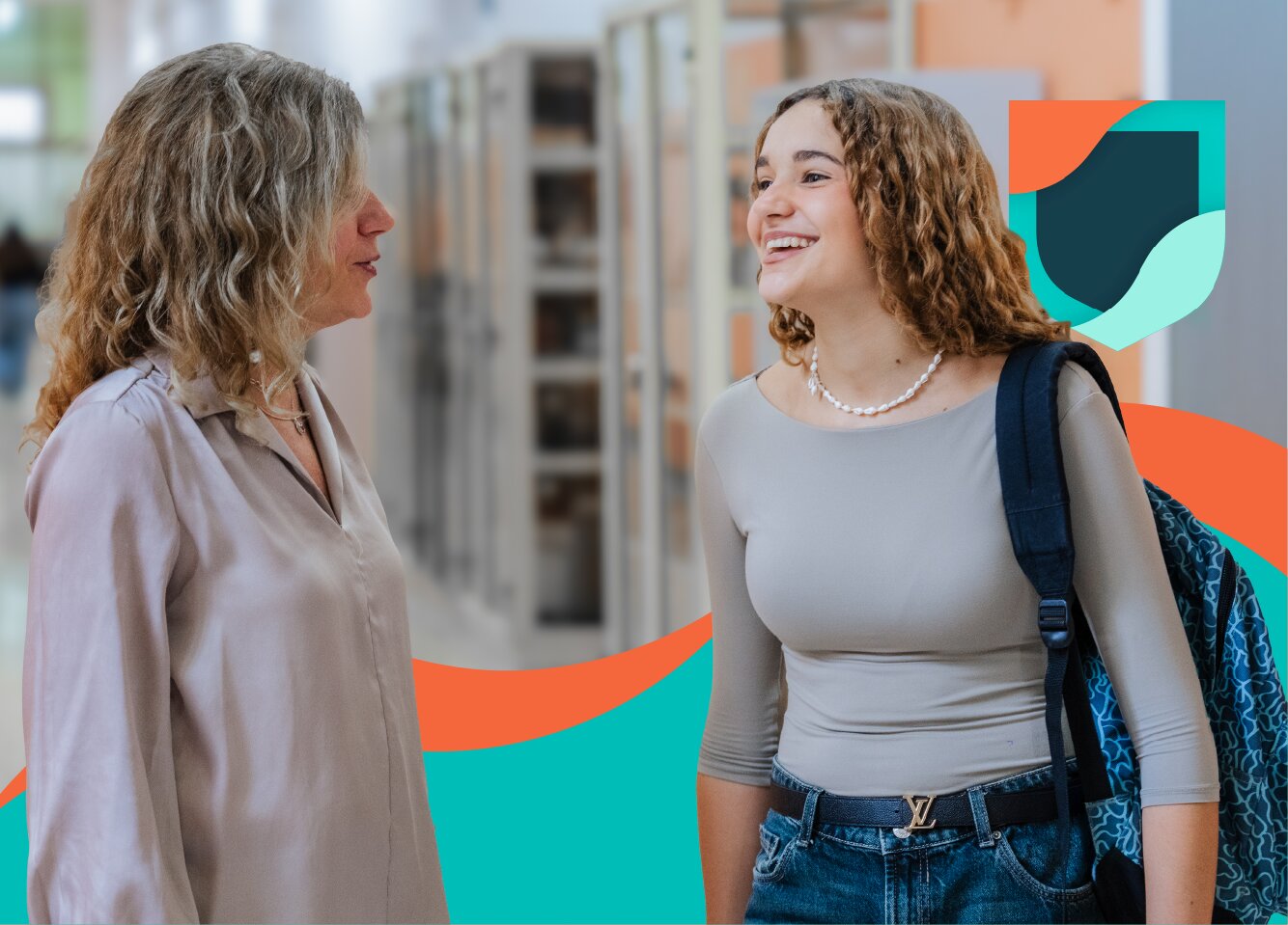 Student with a backpack talking with a teacher in a school hallway.