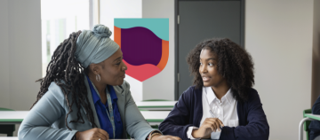 Teacher and student sitting at a desk in a classroom.