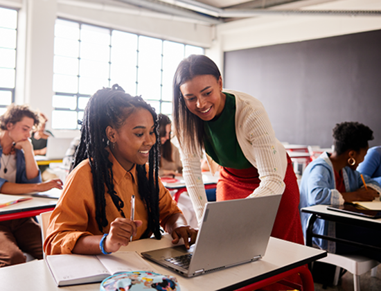 Teacher supports student with laptop at Cambridge University table.