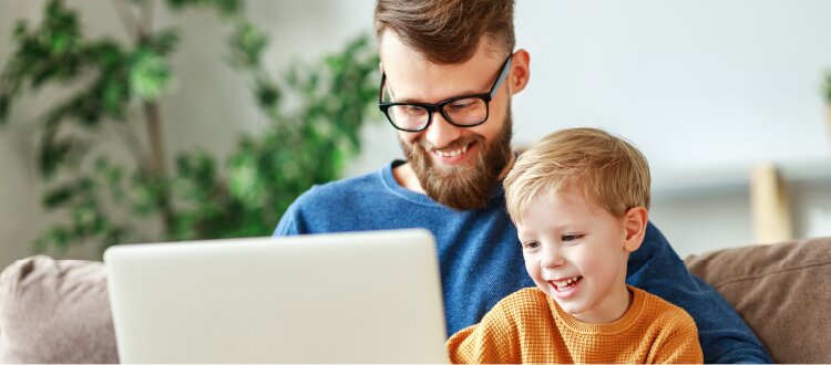 Adult and child sitting together on a sofa, looking at a laptop in a home setting.