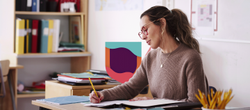 Person writing at a desk with books and papers.