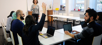 Adult ESOL class with diverse learners using laptops and raising hands
