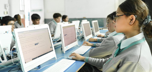 Students working on desktop computers in a classroom during a computer-based activity or exam.