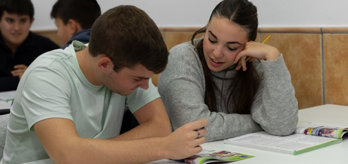Students working together and reading from textbooks in a classroom.