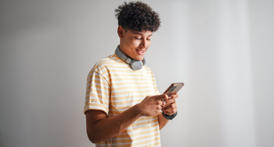Un joven sonríe mientras sostiene un teléfono móvil, listo para hacer una prueba online.